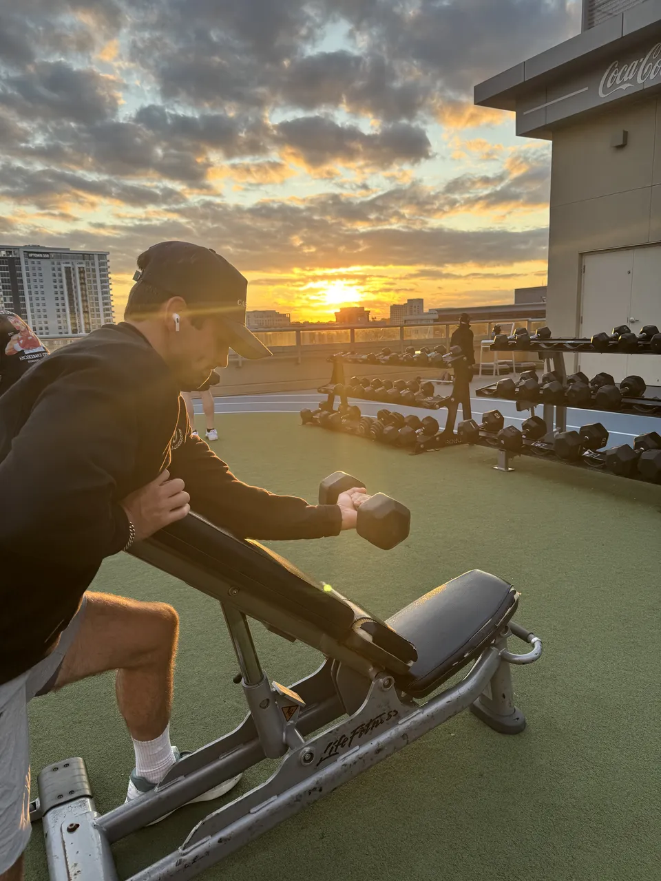 Thomas doing a dumbbell row on a rooftop gym at sunrise