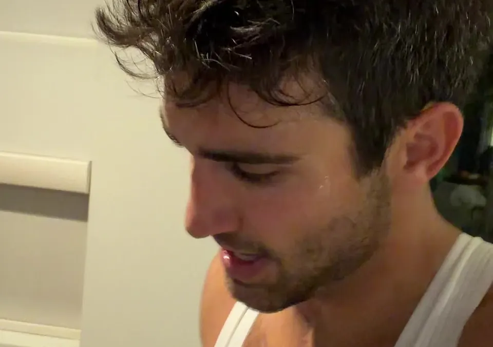 Close-up of Thomas, sweating and looking down mid-session, in a white tank top